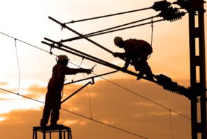 Electricians repairing power lines at sunset, showcasing teamwork and safety.